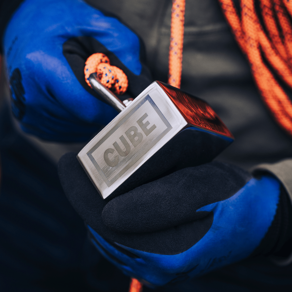 Detailaufnahme Magnetar Cube Bergemagnet in blauen Schutzhandschuhen mit befestigtem Seil, ideal für starkes Magnetfischen.